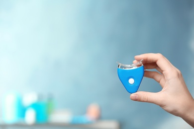 Woman holding teeth whitening device on blurred background. Space for text