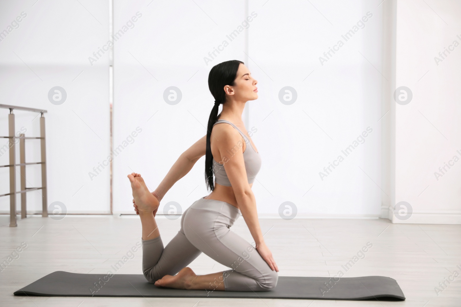 Photo of Young woman practicing One Legged King Pigeon asana in yoga studio. Eka Pada Rajakapotasana pose