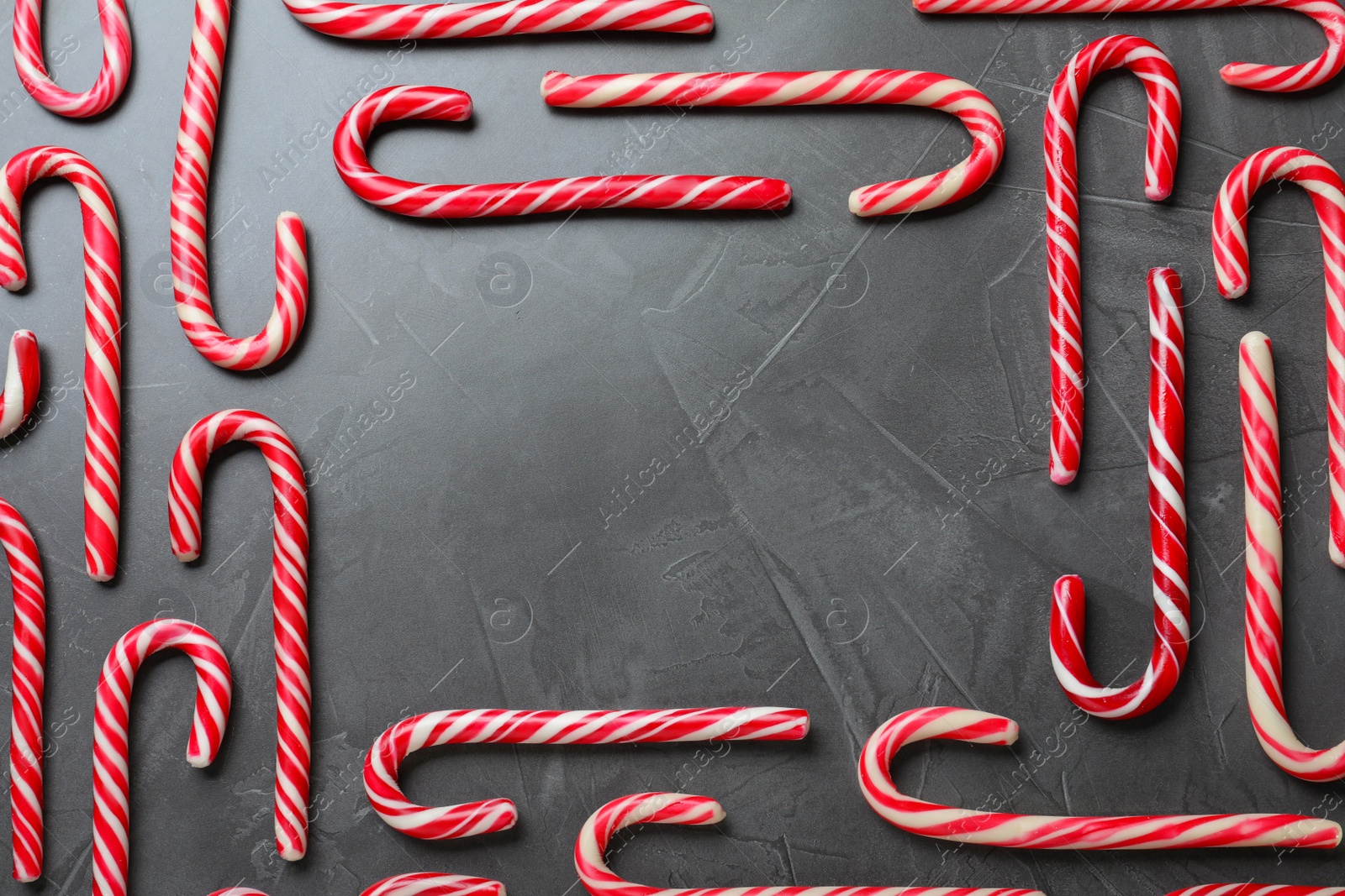Photo of Frame of sweet Christmas candy canes on grey background, flat lay. Space for text