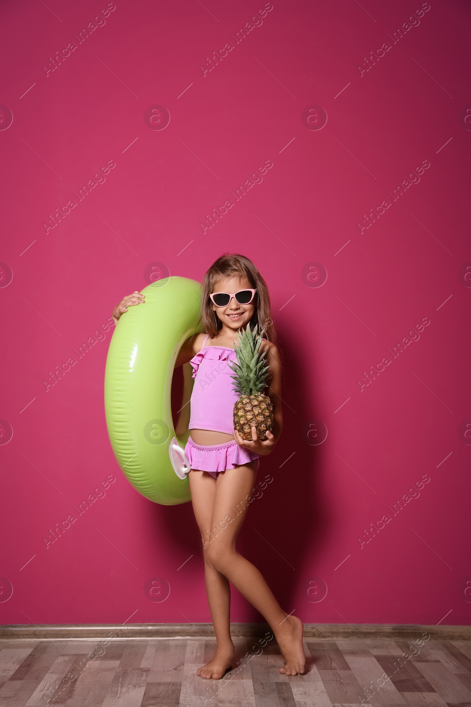 Photo of Cute little girl with pineapple and bright inflatable ring near color wall