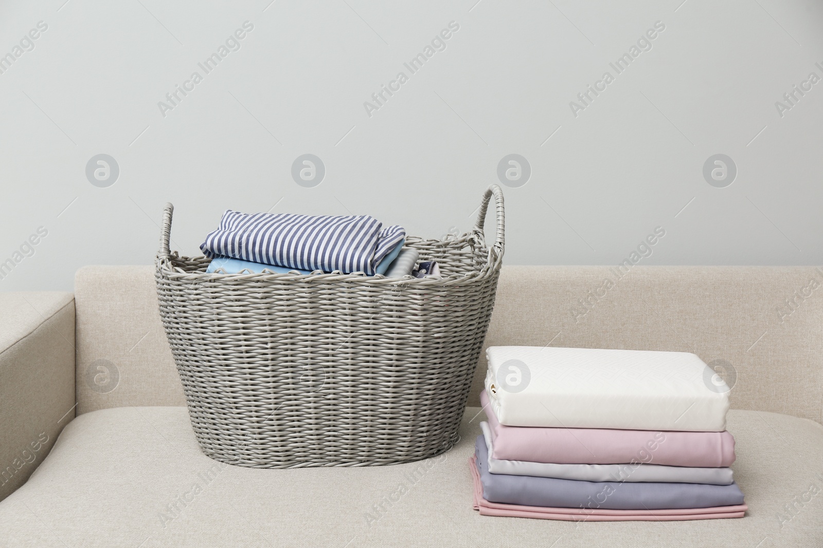 Photo of Laundry basket with clean clothes on sofa indoors