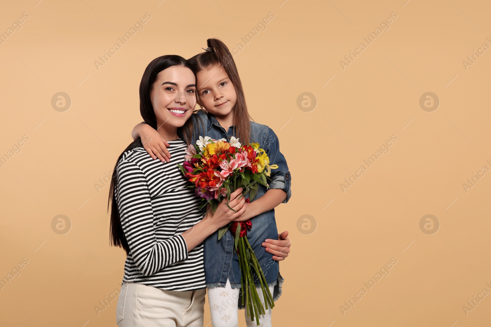 Photo of Happy woman with her cute daughter and bouquet of beautiful flowers on beige background, space for text. Mother's day celebration