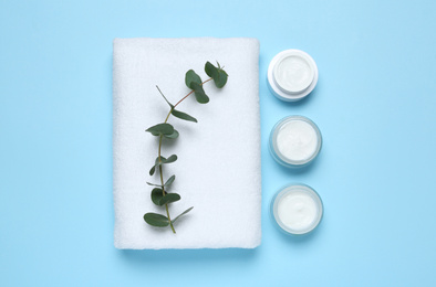 Jars with cosmetic products and towel on light blue background, flat lay