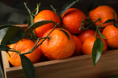 Photo of Fresh ripe tangerines with green leaves in wooden crate, closeup