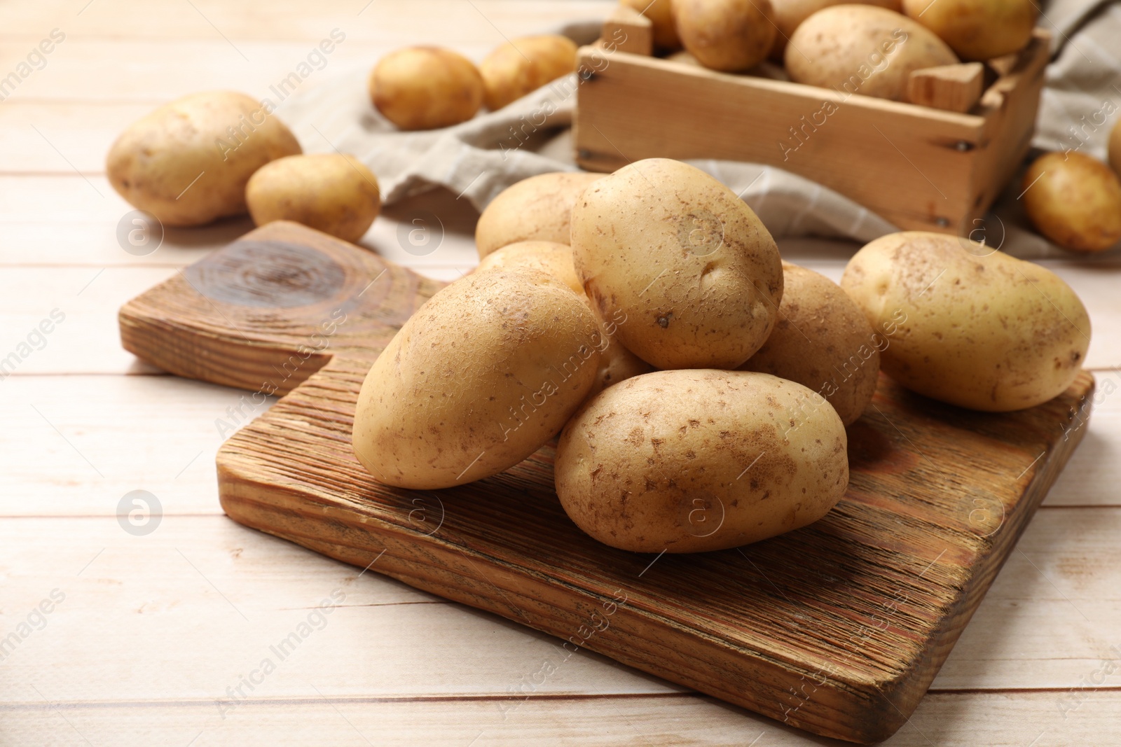 Photo of Raw fresh potatoes and cutting board on light wooden table