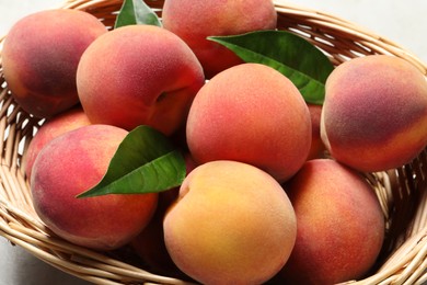 Fresh peaches and leaves in wicker basket on table, closeup