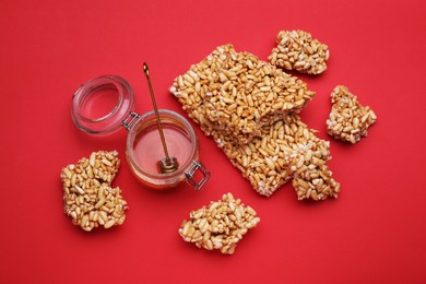 Photo of Puffed rice bars (kozinaki) and honey on red background, flat lay