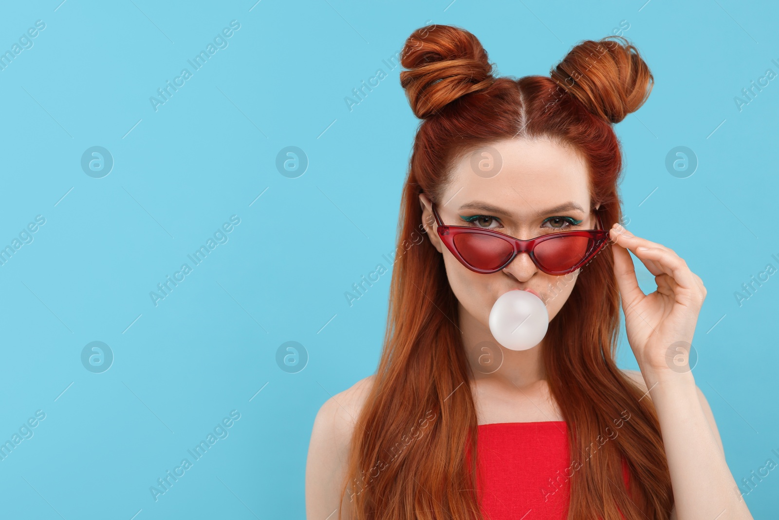 Photo of Beautiful woman in sunglasses blowing bubble gum on light blue background. Space for text