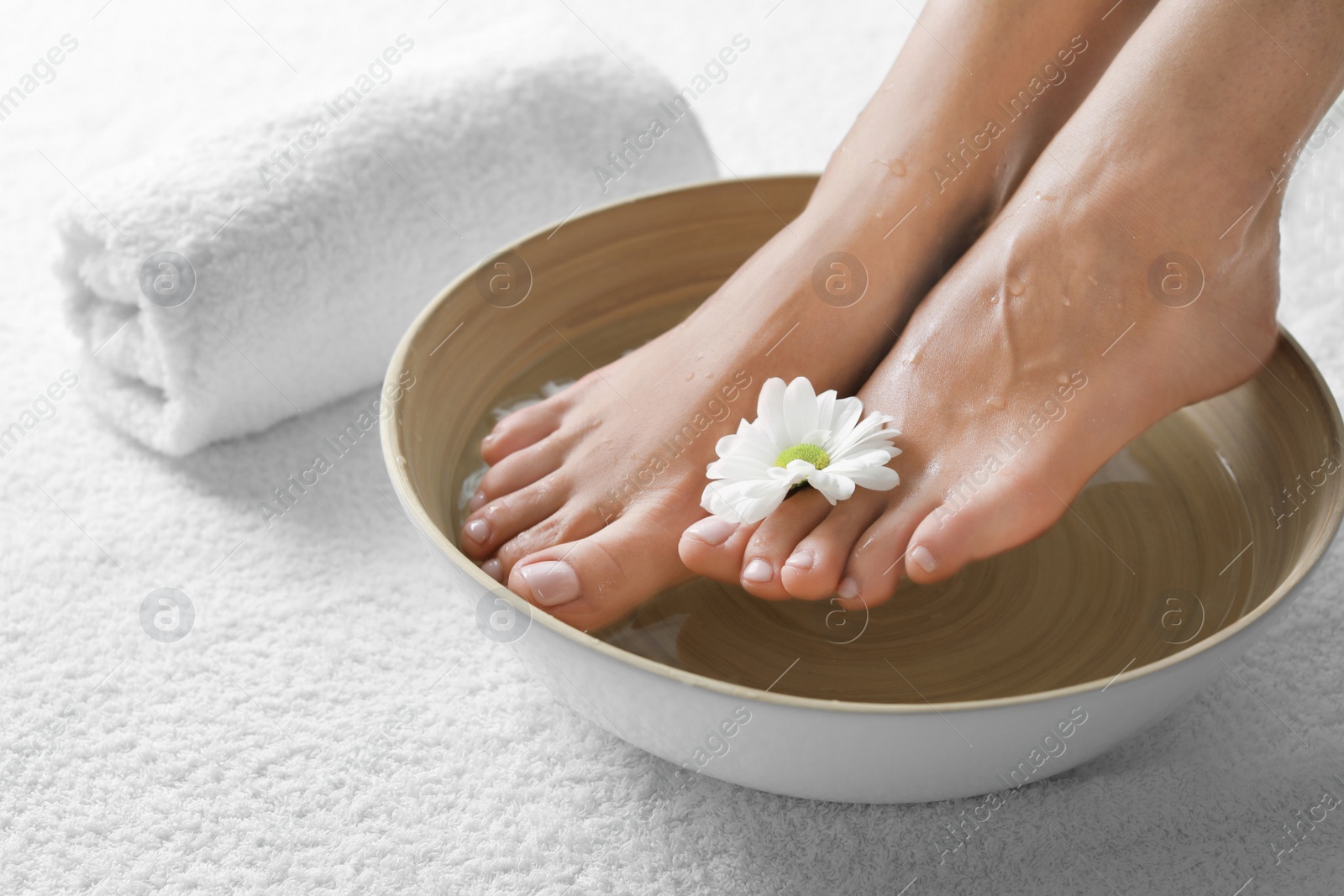 Photo of Closeup view of woman soaking her feet in dish with water and flower on white towel, space for text. Spa treatment