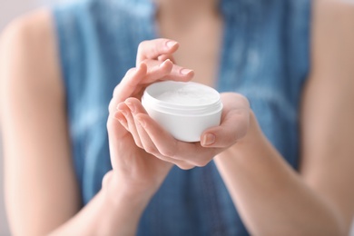 Photo of Young woman holding jar with hand cream, closeup