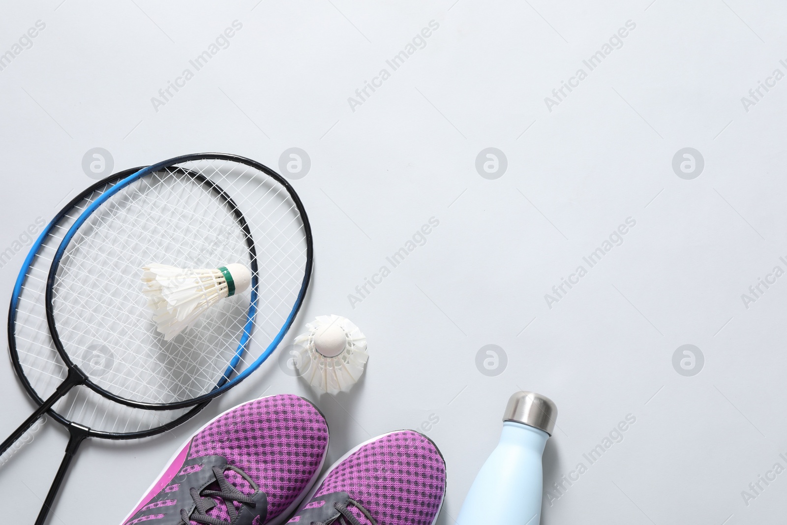 Photo of Feather badminton shuttlecocks, rackets, sneakers and bottle on gray background, flat lay. Space for text