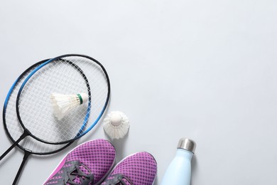Photo of Feather badminton shuttlecocks, rackets, sneakers and bottle on gray background, flat lay. Space for text