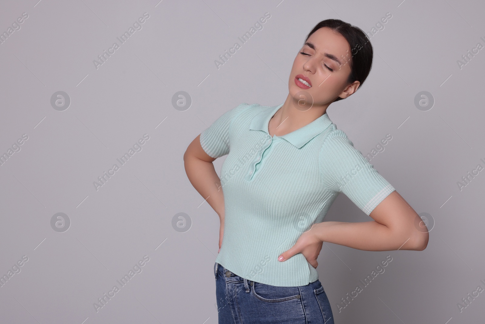 Photo of Young woman suffering from pain in back on light grey background, space for text. Arthritis symptoms
