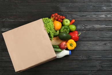 Photo of Overturned paper bag and groceries on black wooden background, top view