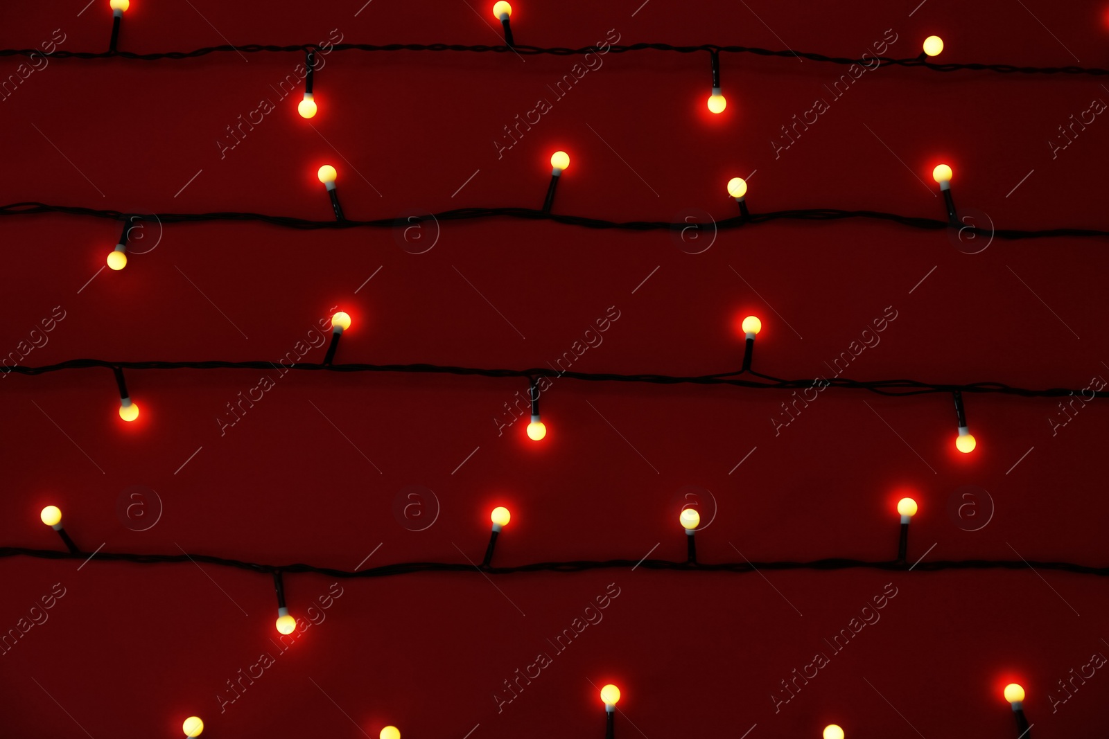 Photo of Glowing Christmas lights on red background, top view