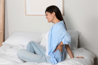 Young woman suffering from back pain while sitting on bed at home. Symptom of scoliosis