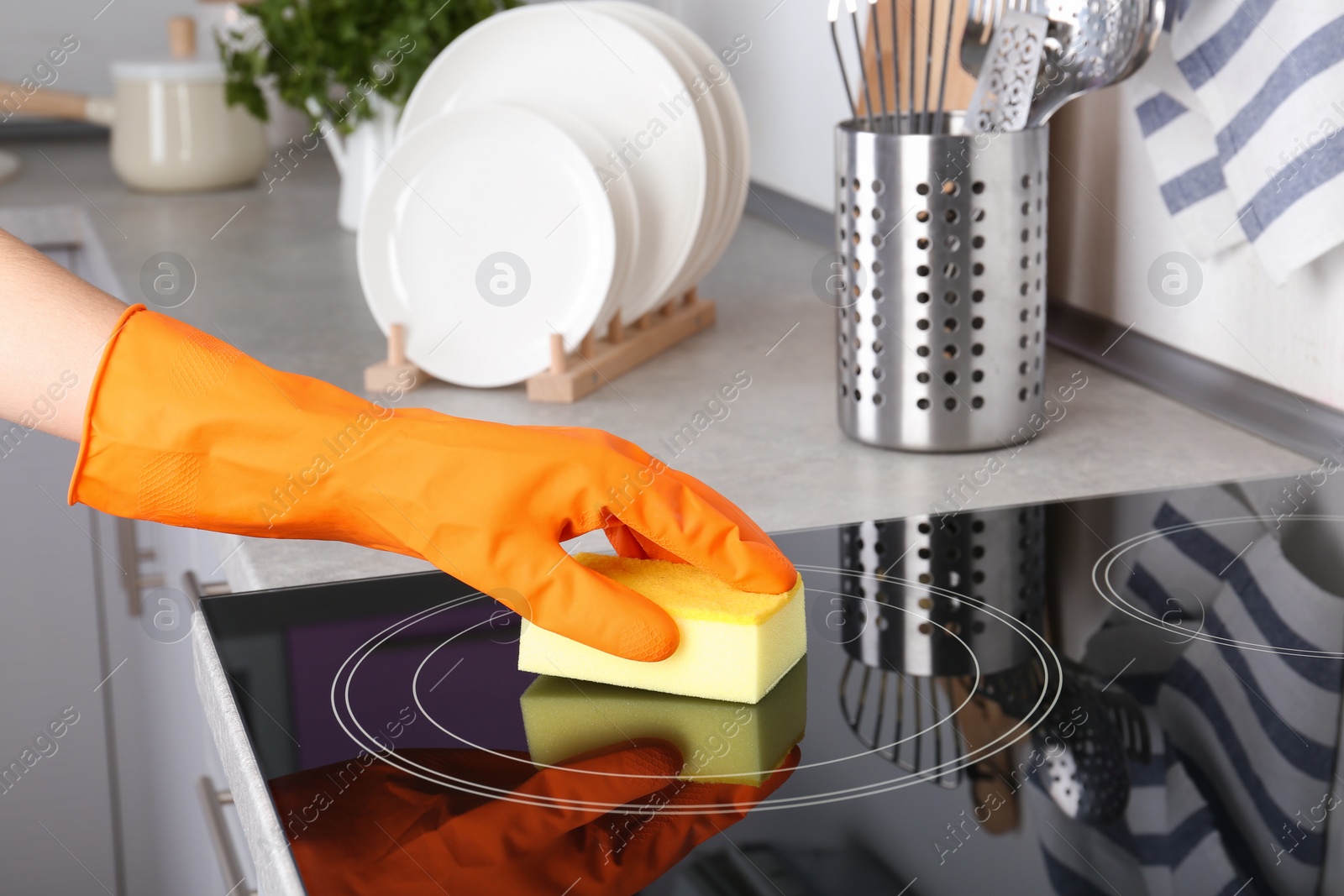 Photo of Woman cleaning oven cooktop with sponge in kitchen, closeup