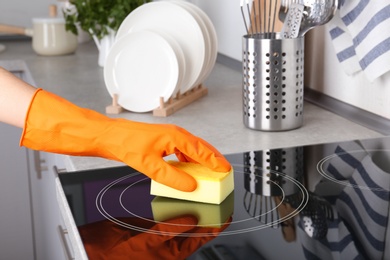 Photo of Woman cleaning oven cooktop with sponge in kitchen, closeup