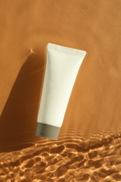 Tube with moisturizing cream in water on orange background, top view