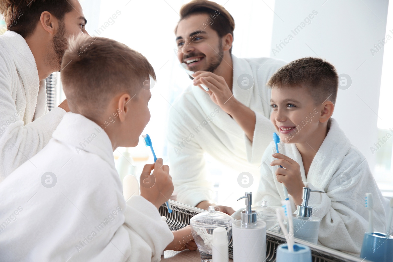 Photo of Young man and his son with toothbrushes near mirror in bathroom. Personal hygiene