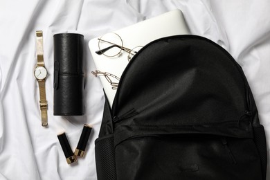 Photo of Stylish urban backpack and different items on white fabric, flat lay