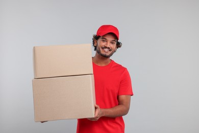 Photo of Happy young courier with parcels on grey background