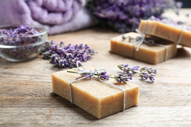 Photo of Handmade soap bars with lavender flowers on brown wooden table, closeup. Space for text