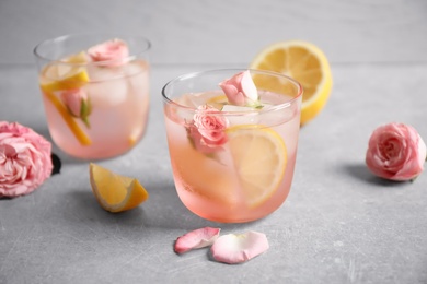 Photo of Tasty refreshing lemon drink with roses on light grey table
