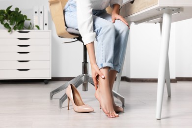 Woman rubbing sore leg in office, closeup