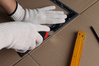 Photo of Worker cutting cardboard with utility knife and ruler, closeup