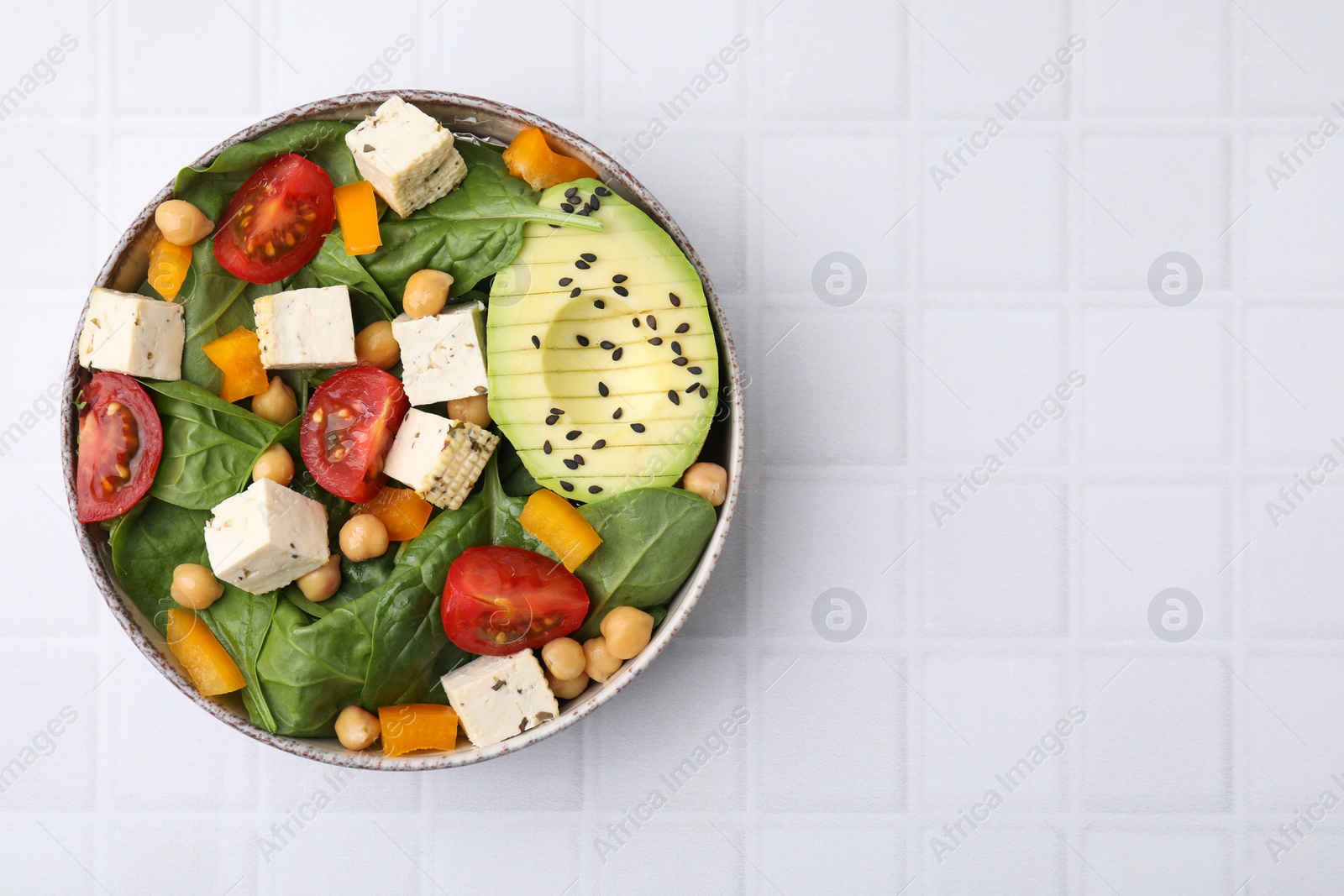 Photo of Bowl of tasty salad with tofu and vegetables on white tiled table, top view. Space for text