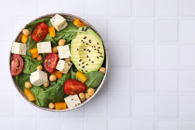 Bowl of tasty salad with tofu and vegetables on white tiled table, top view. Space for text