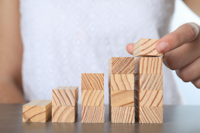 Woman building steps with wooden blocks at grey table, closeup. Career ladder