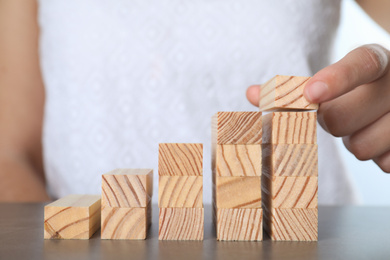 Photo of Woman building steps with wooden blocks at grey table, closeup. Career ladder