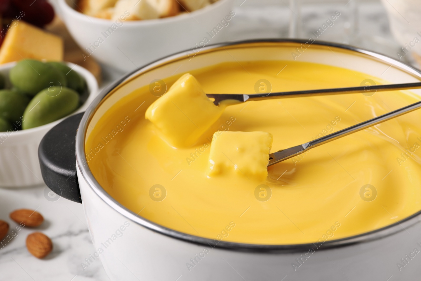 Photo of Pot of tasty cheese fondue and forks with bread pieces on white table, closeup