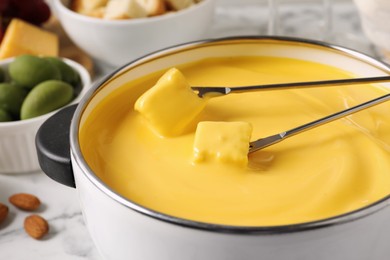 Pot of tasty cheese fondue and forks with bread pieces on white table, closeup