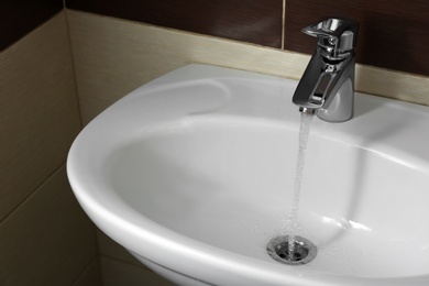 Photo of Closeup view of water flowing from faucet indoors. Space for text