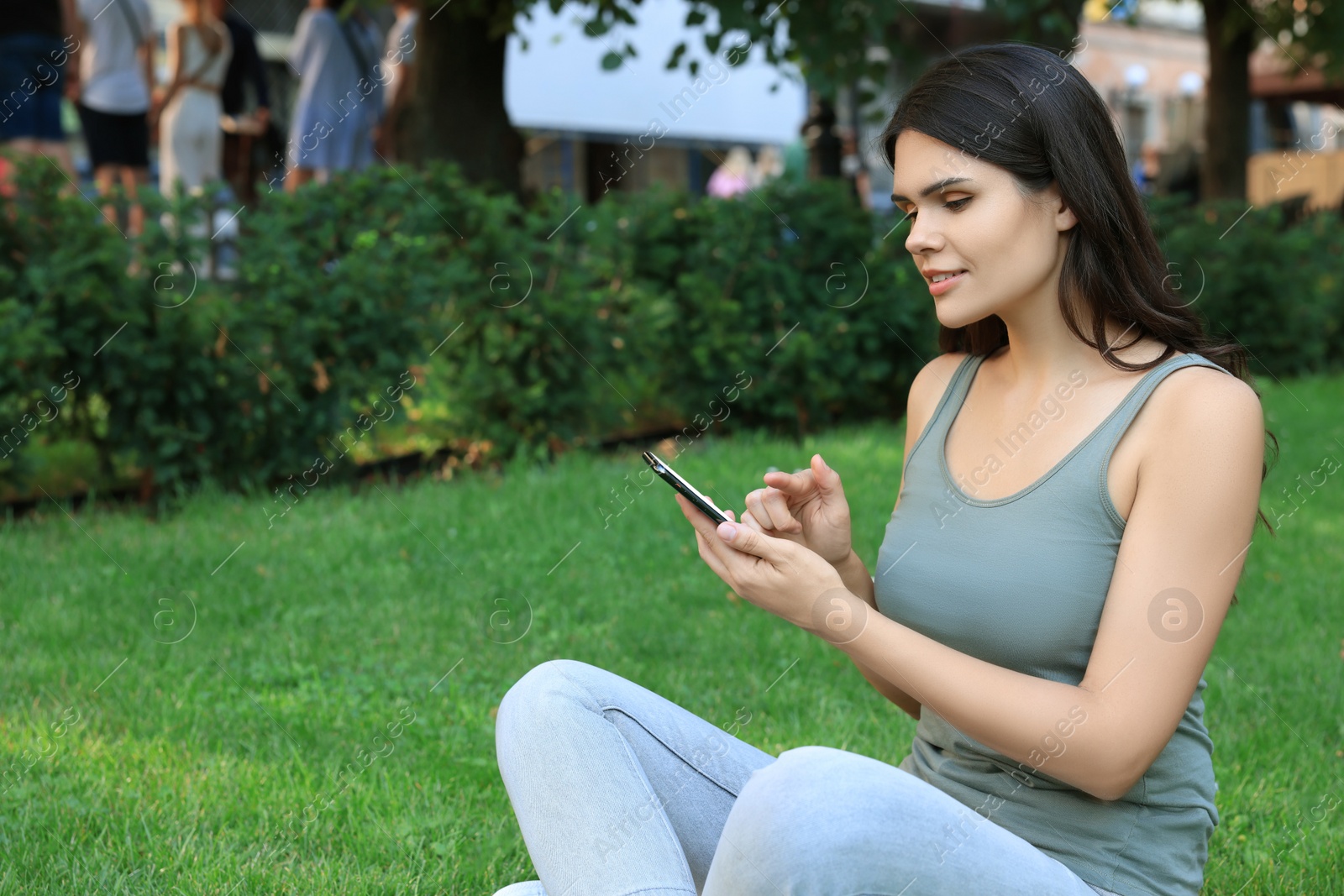 Photo of Young woman using smartphone on green grass in park