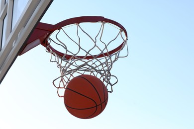 Photo of Basketball ball and hoop with net outdoors on sunny day