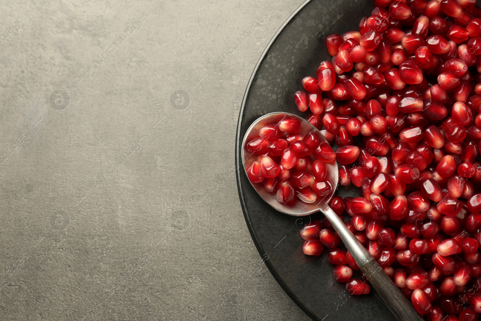 Photo of Ripe juicy pomegranate grains on grey textured table, top view Space for text