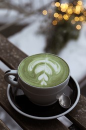 Photo of Cup of fresh matcha latte on wooden bench outdoors in winter