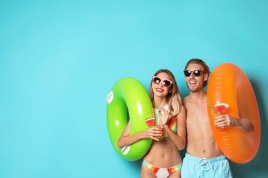 Photo of Happy young couple in beachwear with inflatable rings and cocktails on color background. Space for text