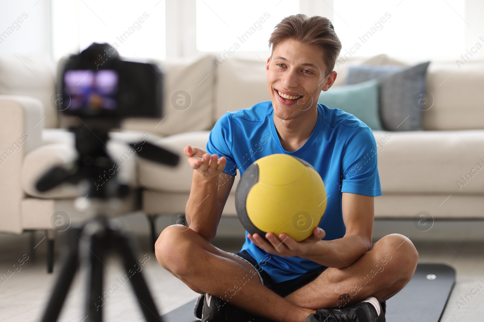 Photo of Smiling sports blogger holding medicine ball while recording fitness lesson with camera at home