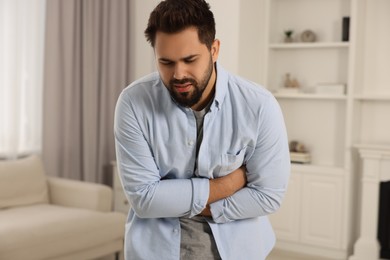 Photo of Young man suffering from stomach pain indoors