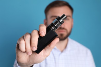 Photo of Man holding electronic cigarette against light blue background, focus on hand