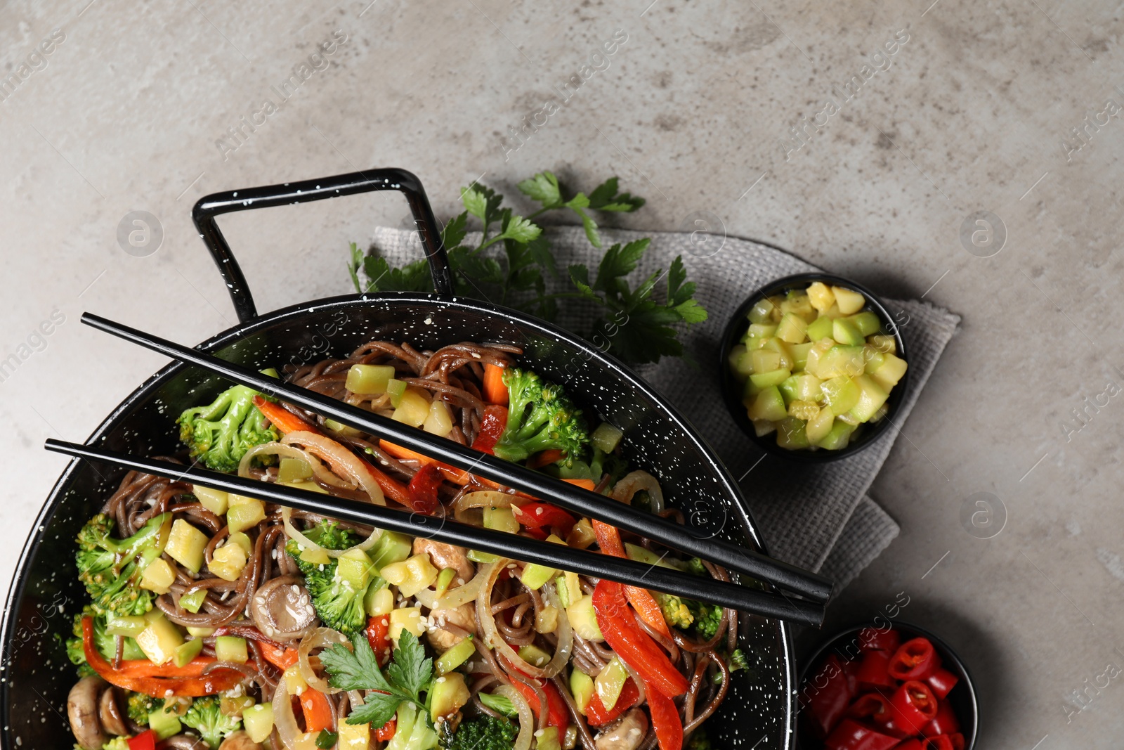 Photo of Stir-fry. Tasty noodles with meat in wok, chopsticks and ingredients on grey textured table, flat lay