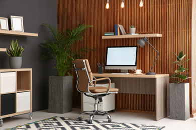 Photo of Comfortable workplace with computer near wooden wall in stylish room interior. Home office design