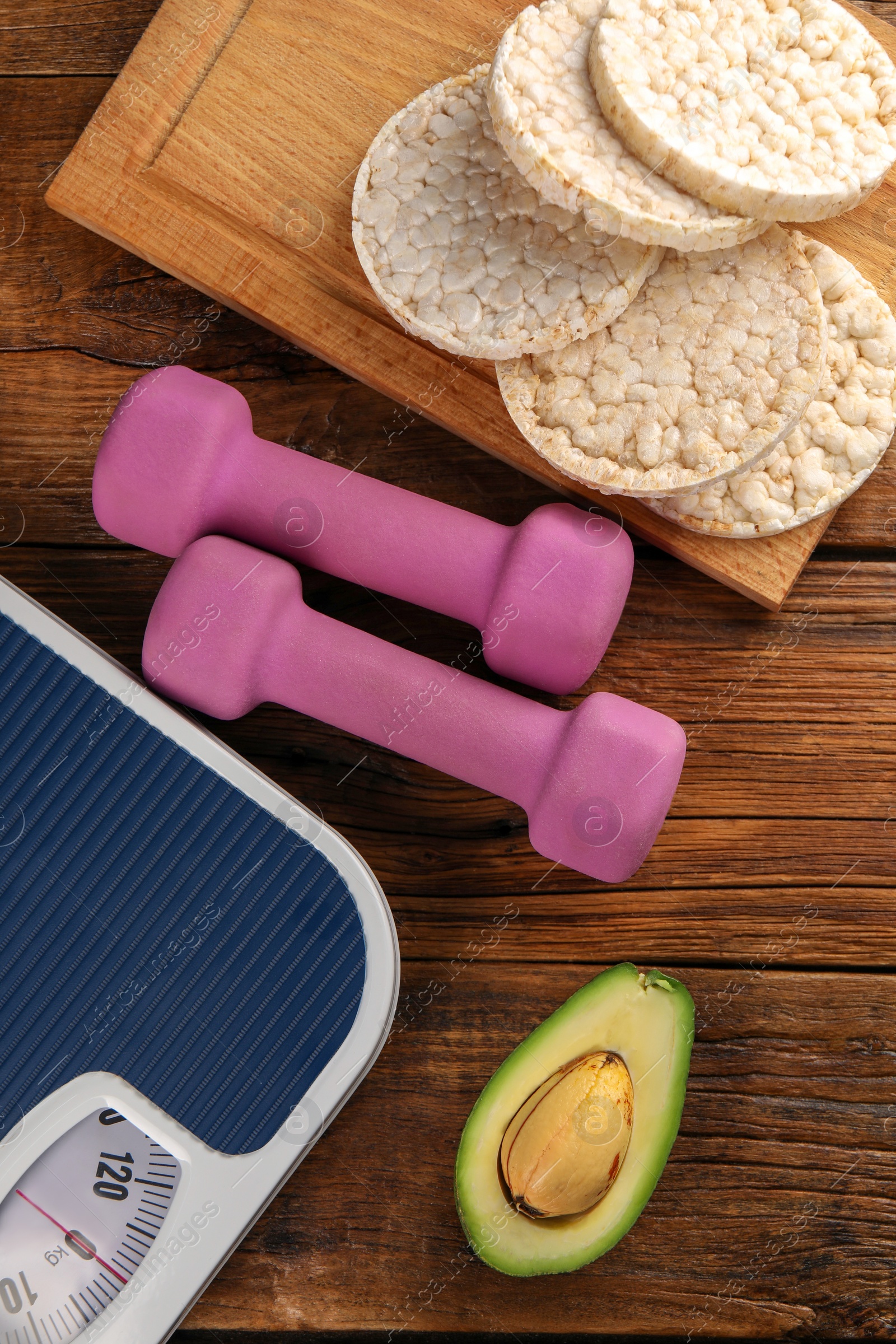 Photo of Healthy diet. Scale, products and dumbbells on wooden table, flat lay