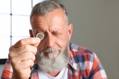 Senior man holding coin indoors, focus on hand. Space for text
