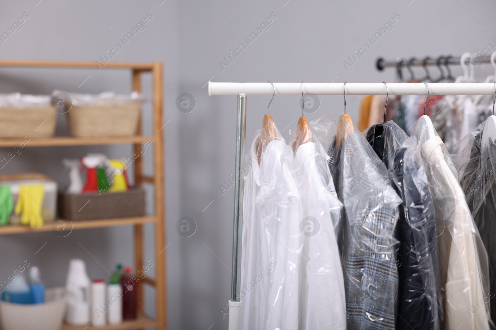Photo of Dry-cleaning service. Hangers with different clothes in plastic bags on rack indoors, space for text